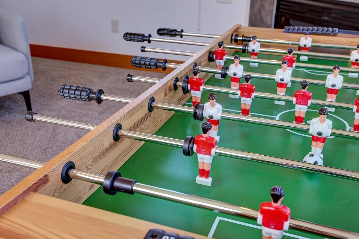 A lively interior shot featuring a foosball table set up for play, with colorful player figures and a welcoming, active vibe. The setting implies family fun, socializing, and multi-generational gatherings indoors.