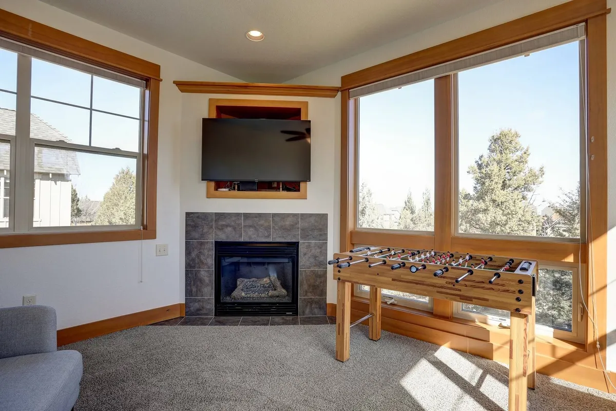 A playful and cozy interior featuring a foosball table, fireplace, large windows, and a television. The space is filled with natural light and offers both entertainment and relaxation opportunities for families or friends.