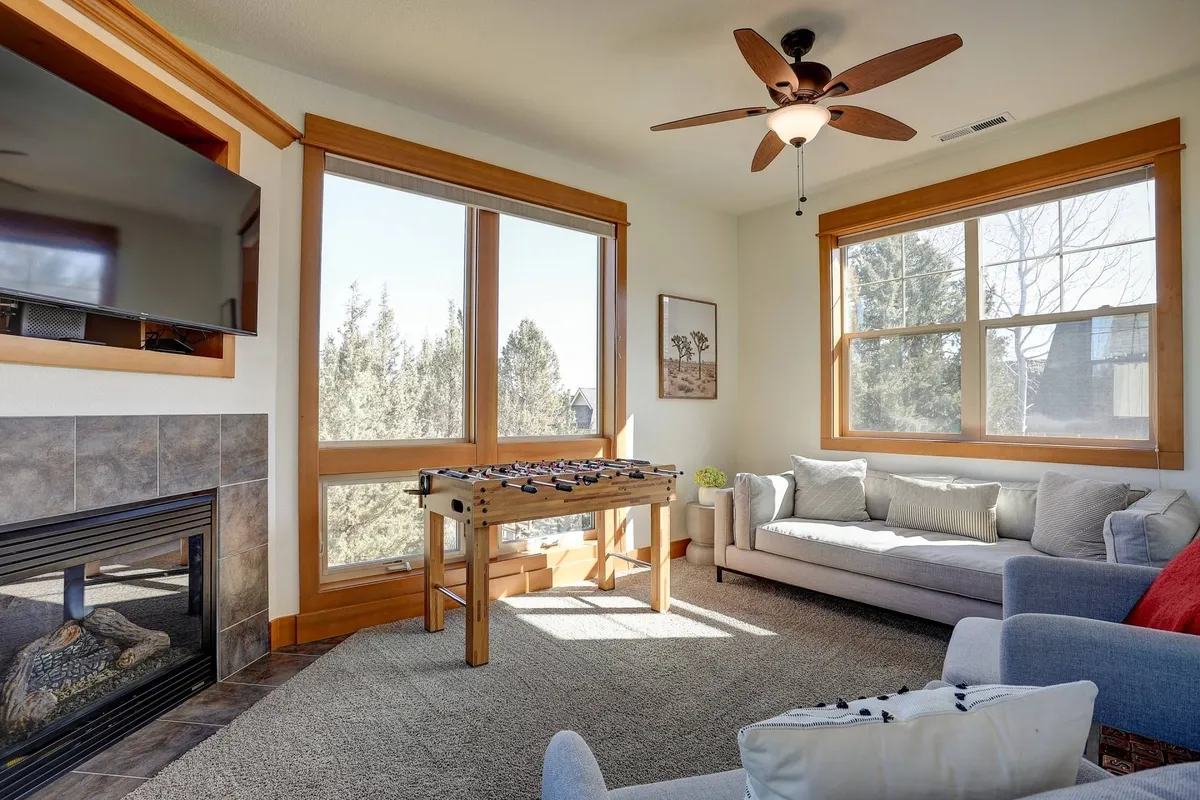A spacious, light-filled bonus room with large windows, a foosball table, a comfortable sofa, and a fireplace. The room offers a blend of relaxation and entertainment options, suitable for both kids and adults.