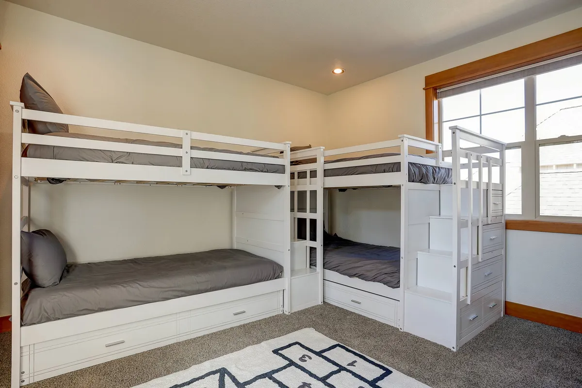 A cheerful bunk room showcasing two sets of twin bunk beds, a colorful rug, and a storage unit. The playful decor is designed for both fun and comfort, perfect for kids' sleepovers or sibling bonding.