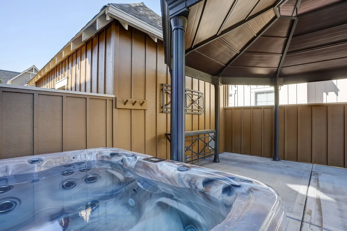 A tranquil view of a private hot tub nestled within a gazebo-like wooden structure, offering privacy and serenity. The soft lighting suggests relaxation, and the design connects the hot tub seamlessly with the surrounding outdoor space.