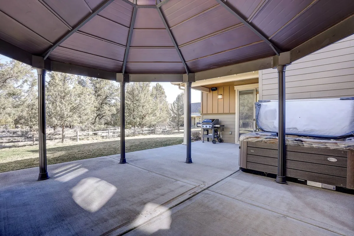 This exterior image showcases a covered gazebo structure that houses a private hot tub and grill, with inviting outdoor seating. The scene is set up for relaxation and entertaining, highlighting both the hot tub and the grilling area in a single, cohesive space.