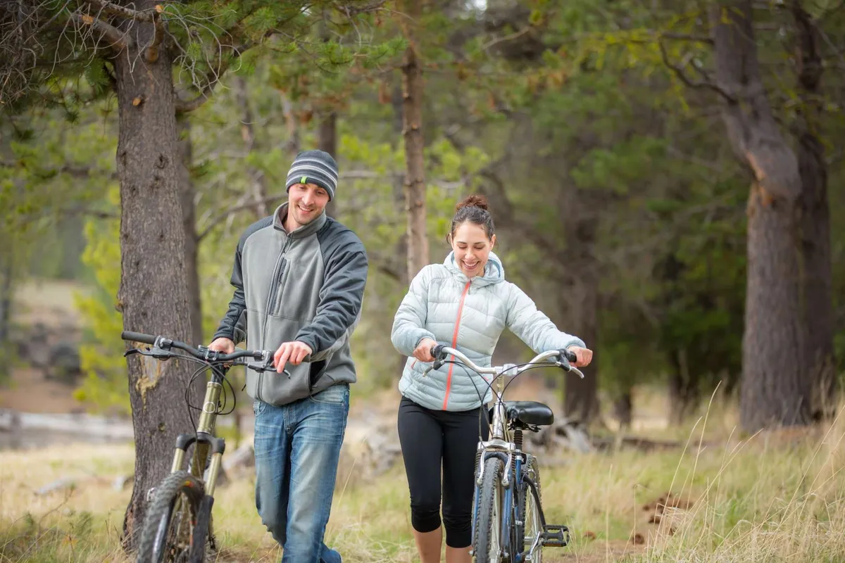 Two people walk their bicycles along a grassy path surrounded by trees, capturing the playful spirit of outdoor exploration. The setting is lush and inviting, suggesting immediate access to trails and nature right outside the property.