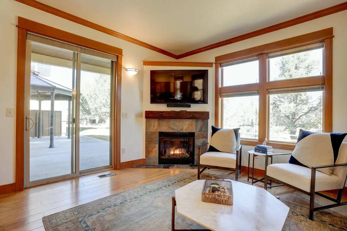 A comfortable living room showcasing a modern fireplace, large windows with abundant natural light, modern chairs, and a central coffee table. The arrangement invites relaxation and cozy evenings.