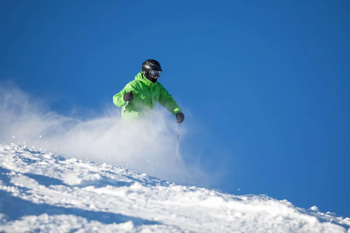 This image depicts a skier carving down a pristine, snow-covered slope under a clear blue sky. The backdrop includes expansive mountain vistas, evoking the thrill and beauty of Central Oregon’s outdoor activities.