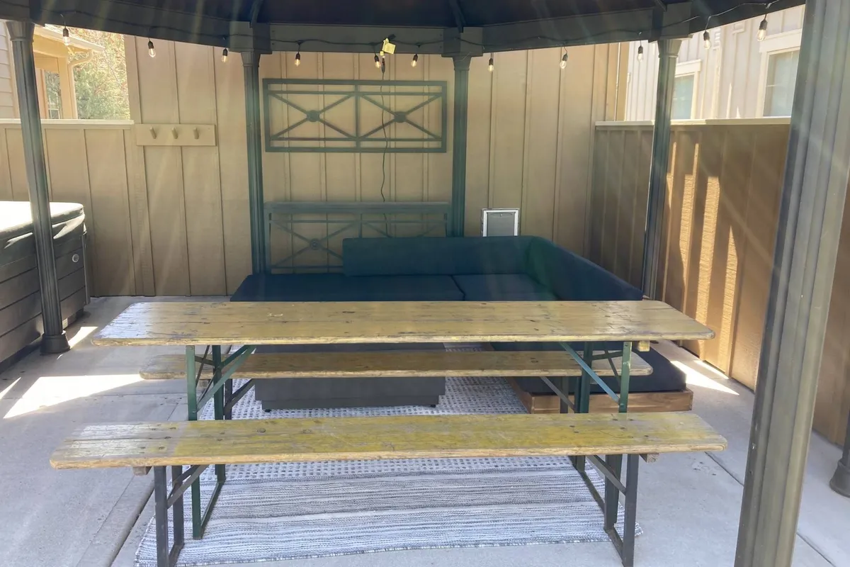 An inviting outdoor seating area features comfortable chairs and a table, a patterned rug, and warm string lights suspended overhead. The space is designed for group relaxation and socializing, with room for both adults and kids to gather and enjoy the fresh air. The setting suggests an easy transition from indoor comfort to outdoor enjoyment, ideal for shared moments and celebrations.