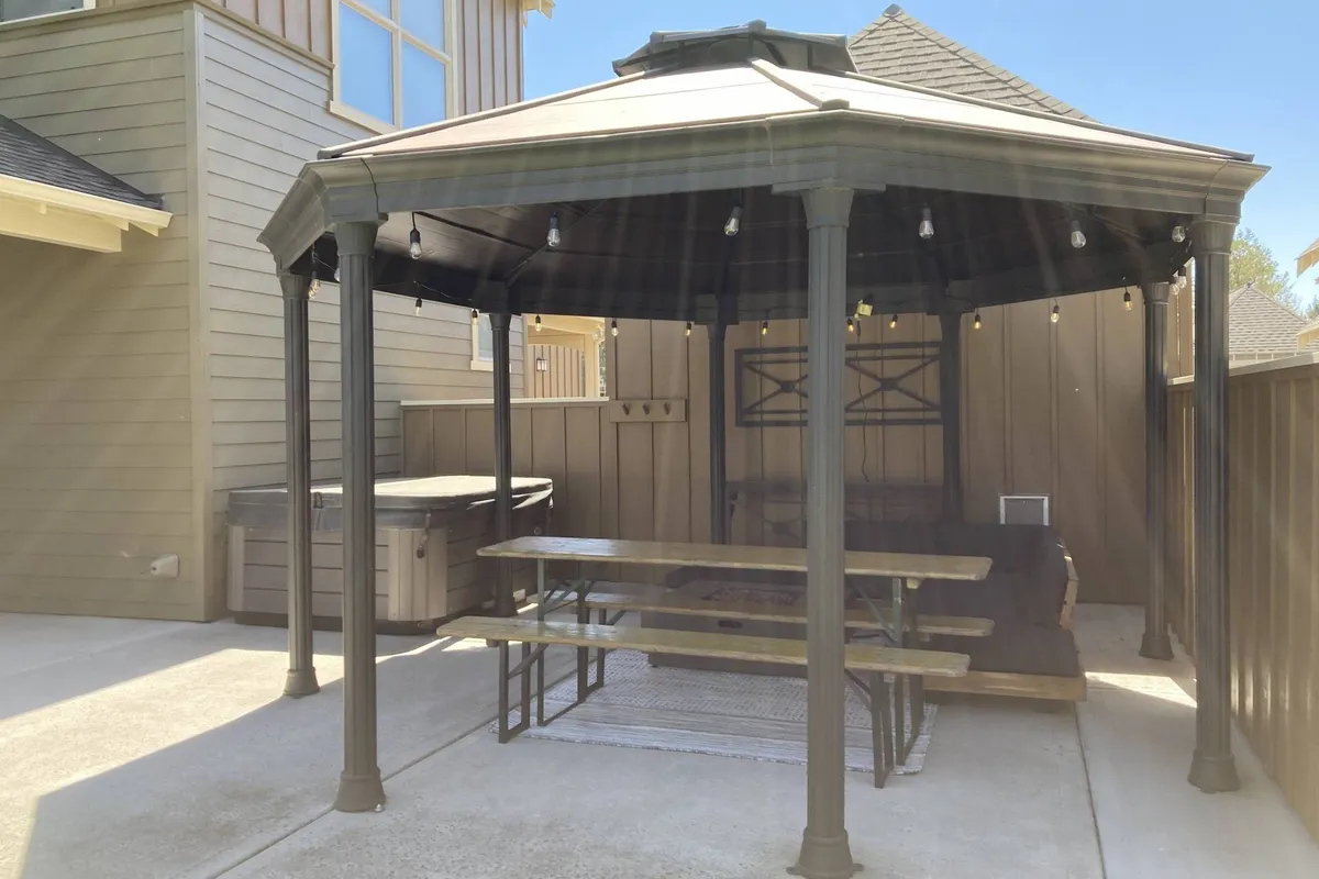 An inviting outdoor living area featuring a gazebo, comfortable seating, and a bubbling hot tub. The setup suggests relaxation and socializing, with the hot tub and covered space ideal for family barbecues or quiet moments after a day of resort activities.